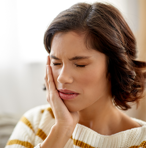 Woman in striped sweater rubbing jaw in pain