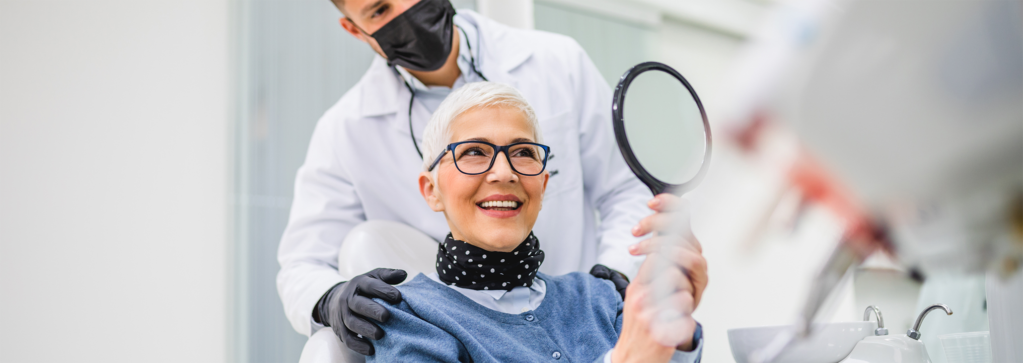 Senior woman with glasses looking at teeth in handheld mirror