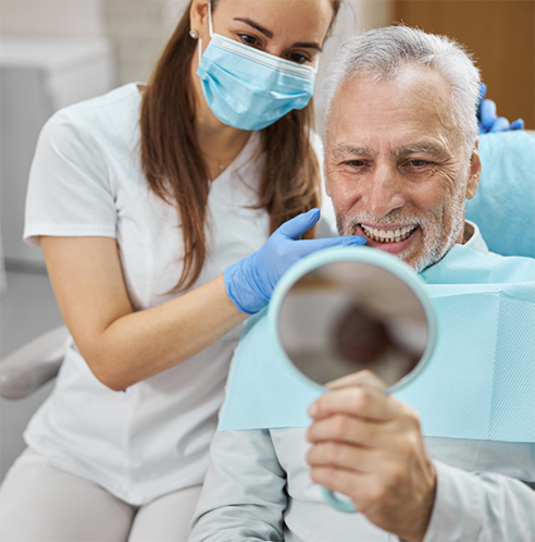 Male patient checking smile in mirror while dentist watches