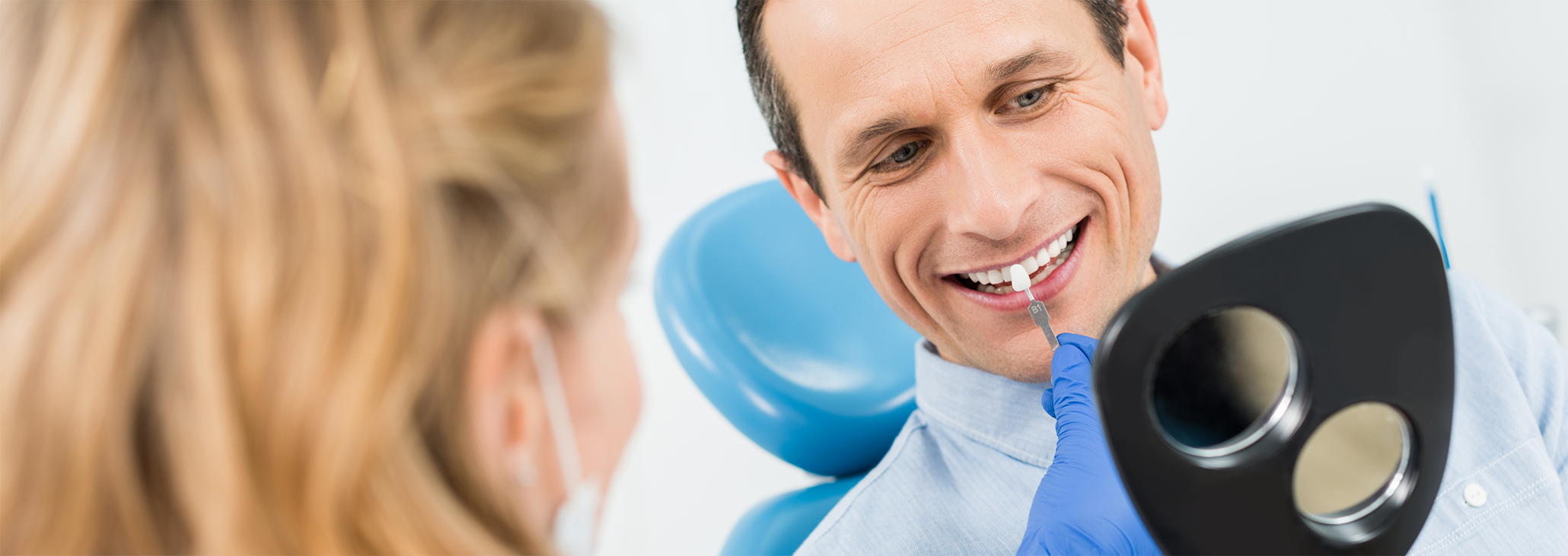 Man looking at handheld mirror while having teeth shade-matched