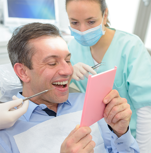 Man looking at smile in mirror during dental treatment