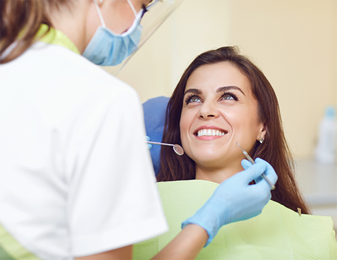Woman sitting in dental chair and smiling up at dentist