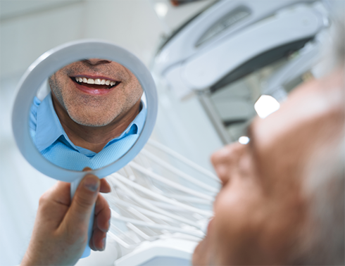Man in dental chair checking smile in mirror