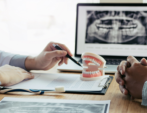Dentist and patient at desk with dentist pointing to model of teeth