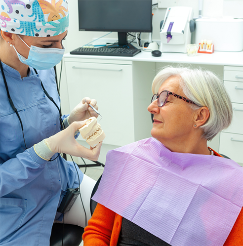 Senior patient looking at model of teeth held by dentist
