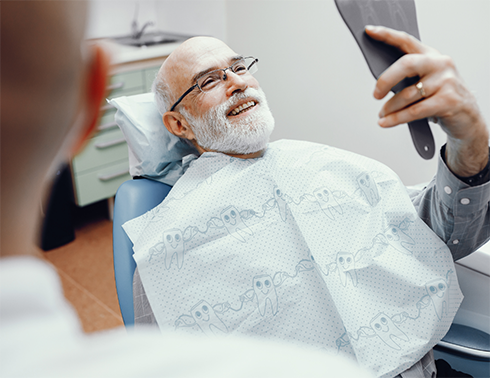 Senior bearded male dental patient checking smile in handheld mirror