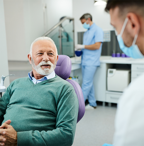 Bearded male dental patient in green shirt looking at dentist