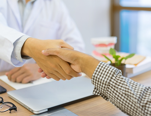 Dentist and patient shaking hands over desk with laptop