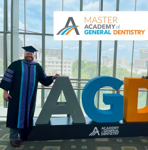 Dr. Boyles in graduation outfit leaning against AGD logo