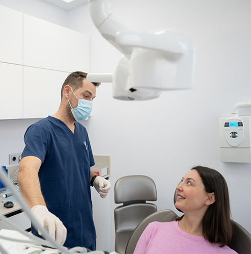 Dentist with face mask speaking to female dental patient