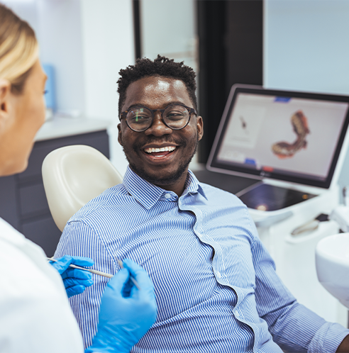 Man with glasses sitting in dental chair smiling