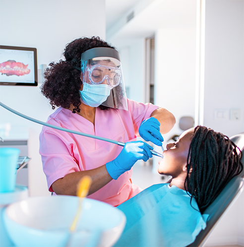 Dentist with facial mask and shield performing tooth extraction