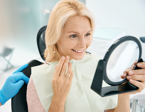 Older woman checking smile in mirror after receiving veneers in Midland