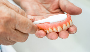 closeup of hands brushing dentures