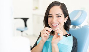 smiling woman holding clear aligners in the dentist chair