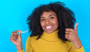 smiling woman holding a clear aligner and giving a thumbs up