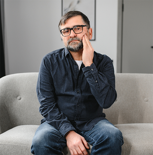 Man with glasses sitting on couch with jaw pain
