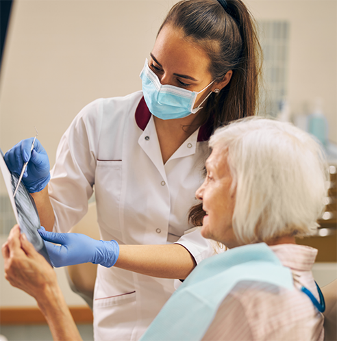 Female dentist with mask showing X ray to senior female patient