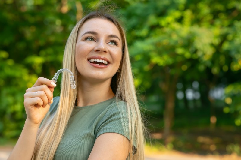 smiling young woman holding a clear aligner outside