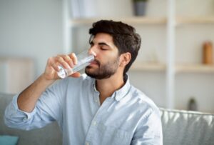 man drinking water on a couch at home